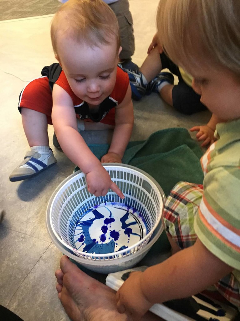 Infants spin paint in a salad spinner.